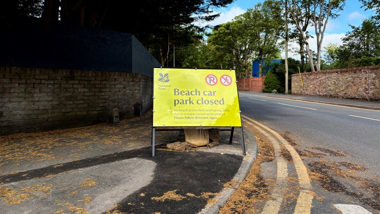 Bright yellow sign with the text Formby beach car park closed for a major conservation project until spring 2026. Also shows no parking or pedestrian access symbols